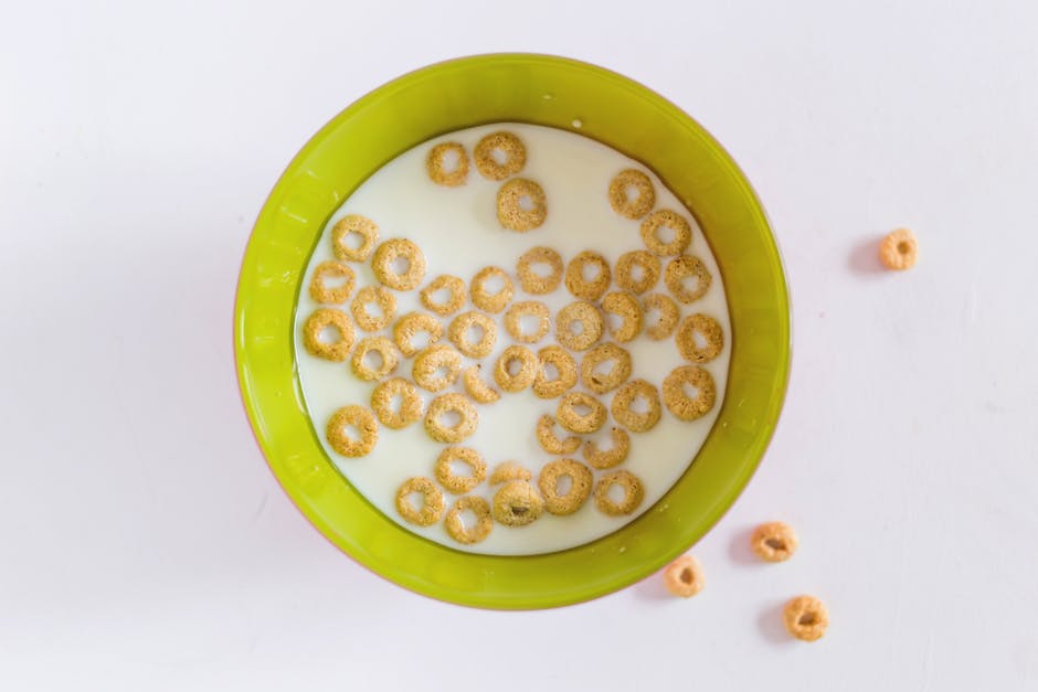 A green ceramic bowl filled with cereal rings floating in milk, positioned on a white surface. Several cereal pieces are scattered outside the bowl on the surface. The scene depicts a breakfast setting, with the cereal and milk clearly visible, and the bowl centrally placed within the image. This simple visual focuses on food presentation, with no transportation or moving elements related to house removals or relocation services, corresponding to the context of Harringay Man and Van's removals page.